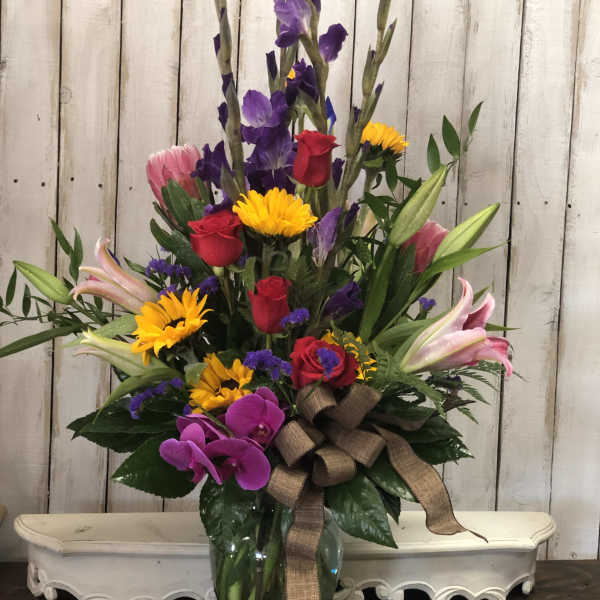 Tall mixed bouquet in a glass vase with roses, lilies, orchids, and yellow daisies