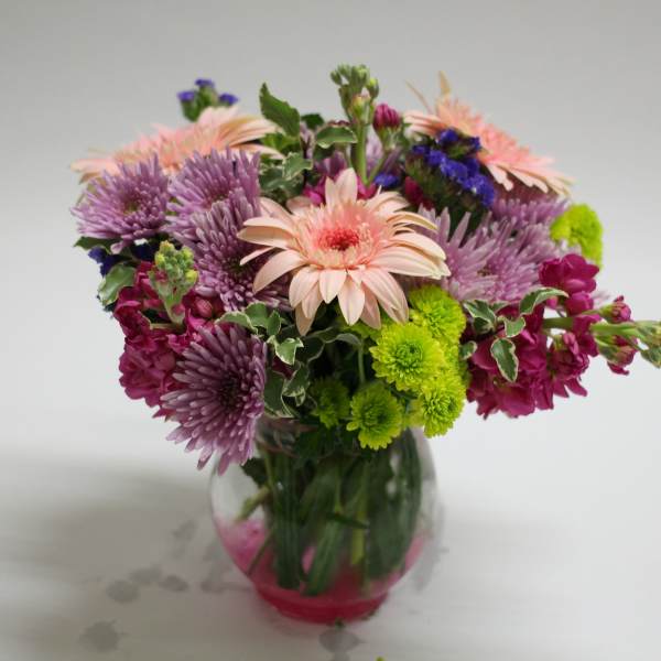 Mixed bouquet of pink, purple, and green flowers in a glass vase
