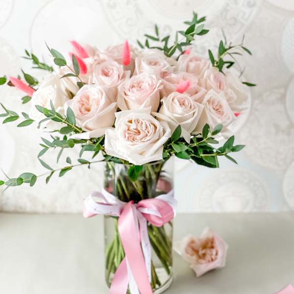 Bouquet of pale pink roses in a glass vase with a pink ribbon