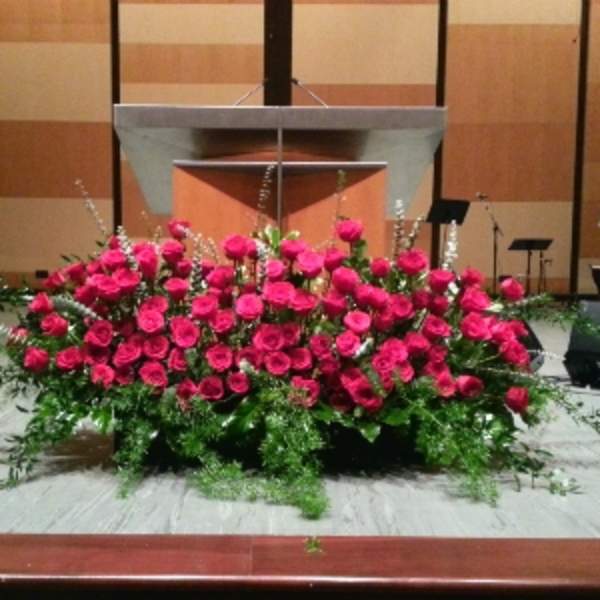 Large low arrangement of bright pink roses with white accent flowers in front of a podium