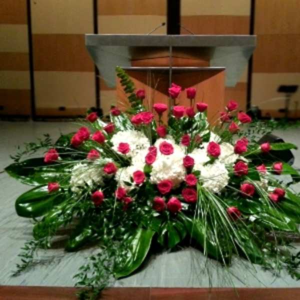Large red rose and white flower spray with abundant foliage arranged in front of a podium