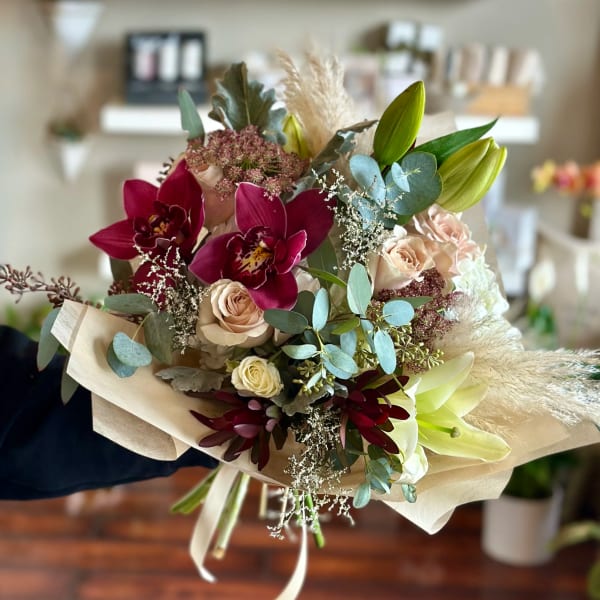 Bouquet of burgundy orchids, pale roses, and lilies wrapped in paper