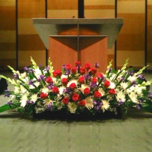 Large red, white, and purple floral spray arranged low in front of a wooden podium.