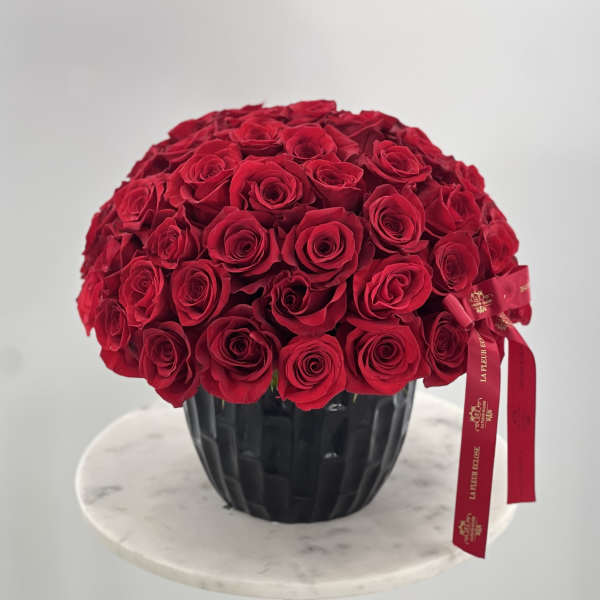 Large bouquet of red roses in a black vase with a red ribbon