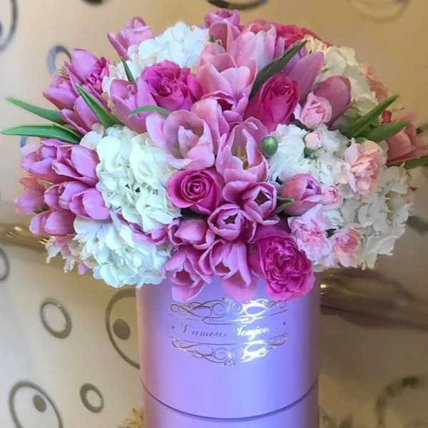 Pink tulips and roses with white hydrangeas arranged in a lavender round hatbox.