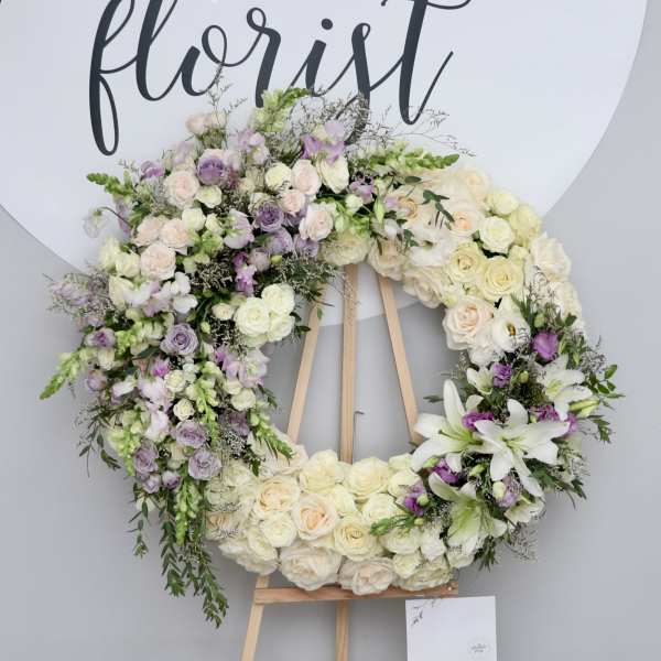 Large floral wreath on a wooden easel with white, cream, and lavender flowers