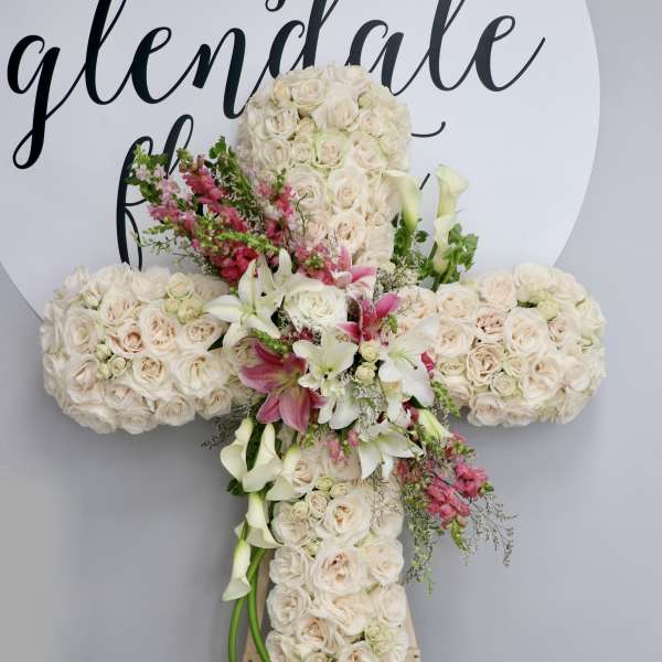 Large floral cross covered in cream roses with pink and white accents