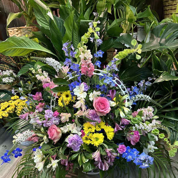 Large mixed floral arrangement with pink roses, yellow daisies, and blue delphinium