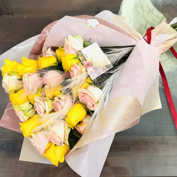 Bouquet of yellow and blush pink roses wrapped in pink paper