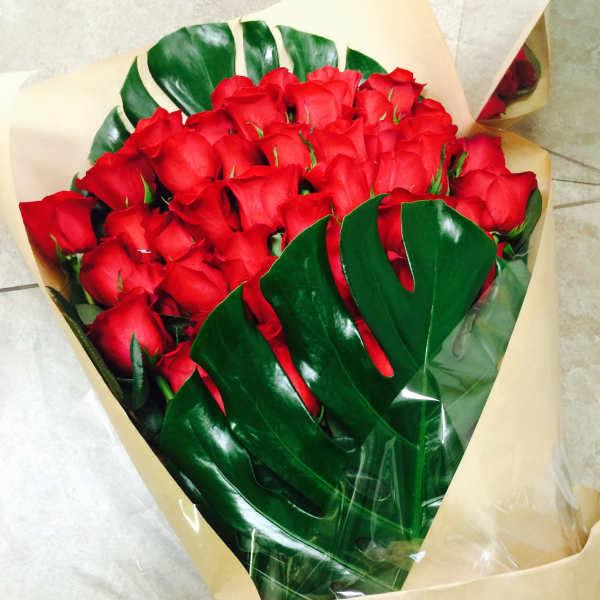 Bouquet of red roses wrapped in tan paper with glossy green leaves