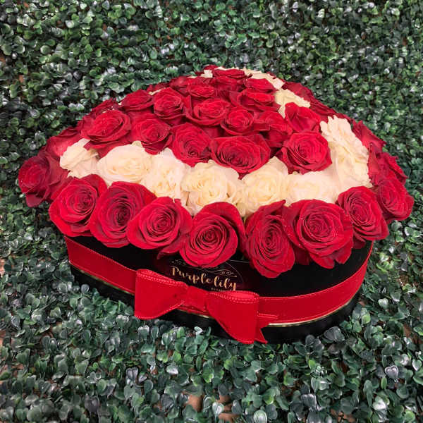 Red and cream roses arranged in a round black box with a red ribbon