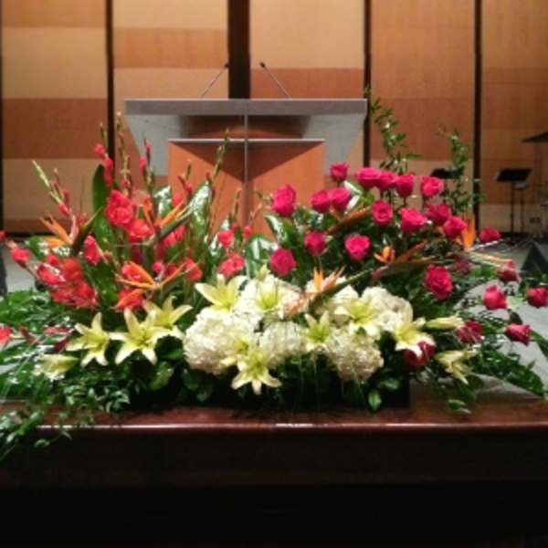 Large altar floral arrangement with pink roses, white hydrangeas, lilies, and tropical blooms.