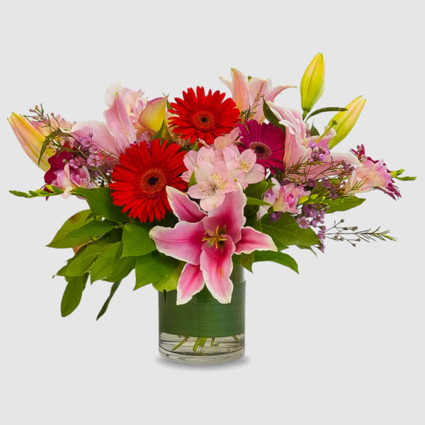 Mixed bouquet of pink lilies, red gerbera daisies, and a glass vase