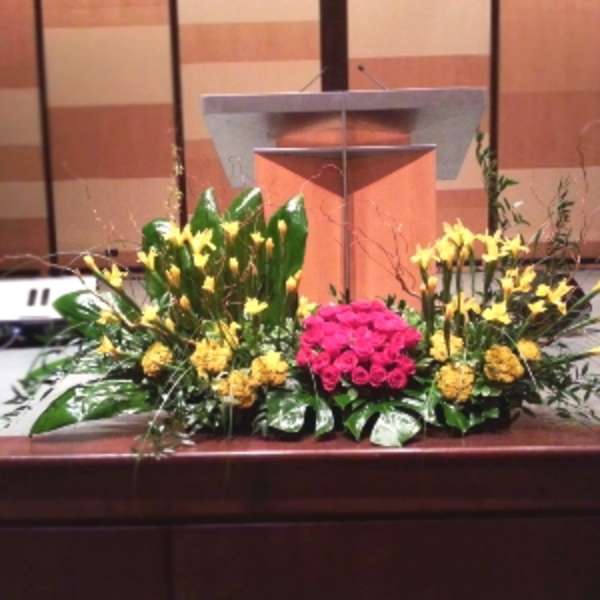 Large altar arrangement of yellow flowers with a central cluster of pink roses before a wooden podium