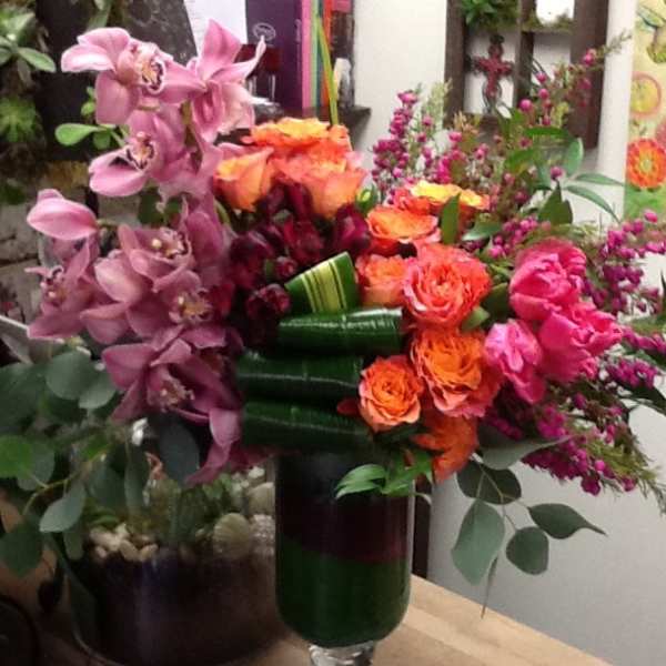 Mixed bouquet with pink orchids, orange roses, and magenta flowers in a glass vase