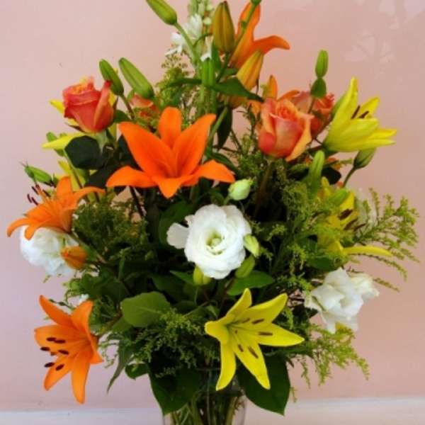 Bouquet of orange and yellow lilies with white blooms in a clear glass vase