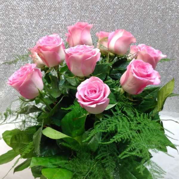 Pink roses arranged in a clear glass vase with greenery