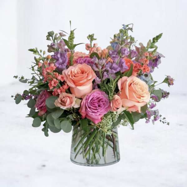 Mixed bouquet of peach and lavender roses with purple accents in a clear glass vase