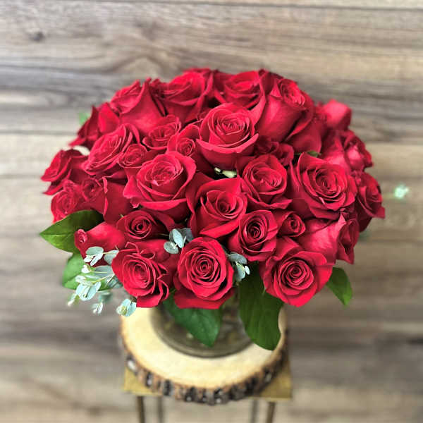 Bouquet of red roses in a glass vase on a wood slice stand