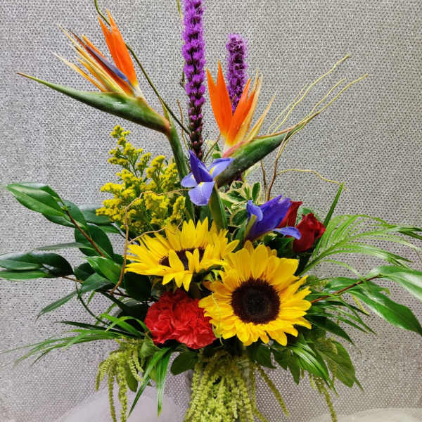 Tropical bouquet with sunflowers, bird of paradise, and purple spikes in a glass vase