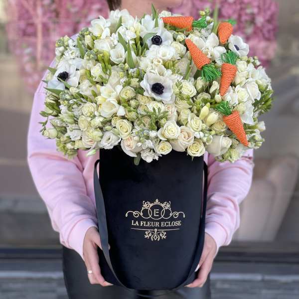 Large white flower arrangement in a black hat box with orange carrot decorations