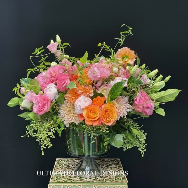 Pink and orange floral arrangement in a glass pedestal vase