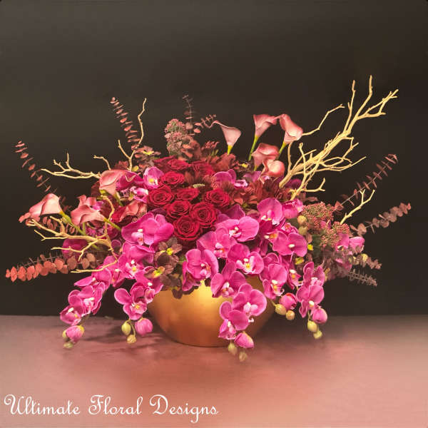 Pink orchids and red roses arranged in a gold bowl