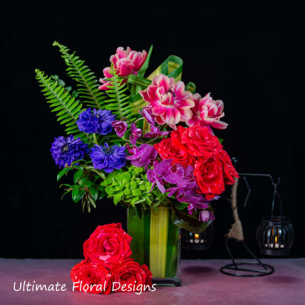 Colorful floral arrangement in a tall green vase with roses and orchids