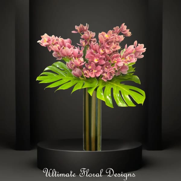 Pink orchid arrangement in a tall glass vase with large tropical leaves