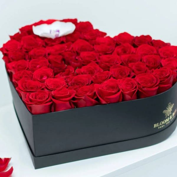 Heart-shaped box filled with red roses and a white accent flower