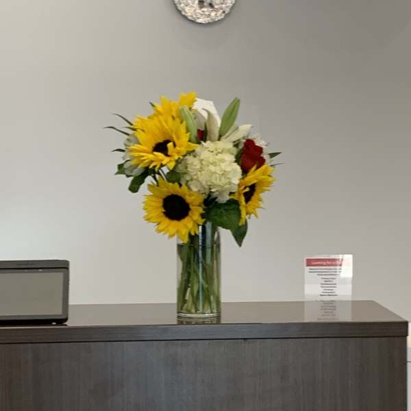 Sunflower bouquet in a tall glass vase with white and red flowers