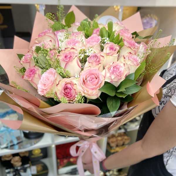 Large hand-tied bouquet of pink and white roses wrapped in pink paper with a satin ribbon bow.