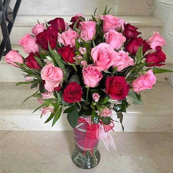 Tall vase of pink and red roses with pink filler flowers and ribbon on a marble step