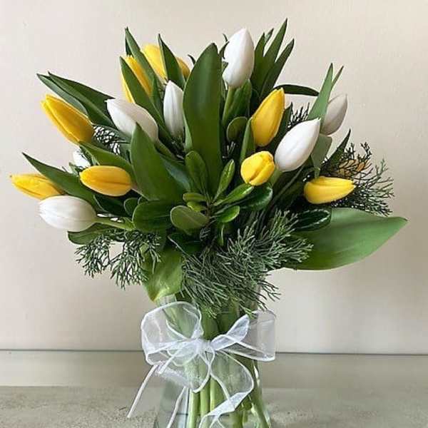 Yellow and white tulips arranged in a clear glass vase with a white ribbon bow