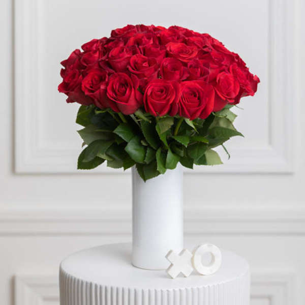 Red roses arranged in a white vase with green leaves