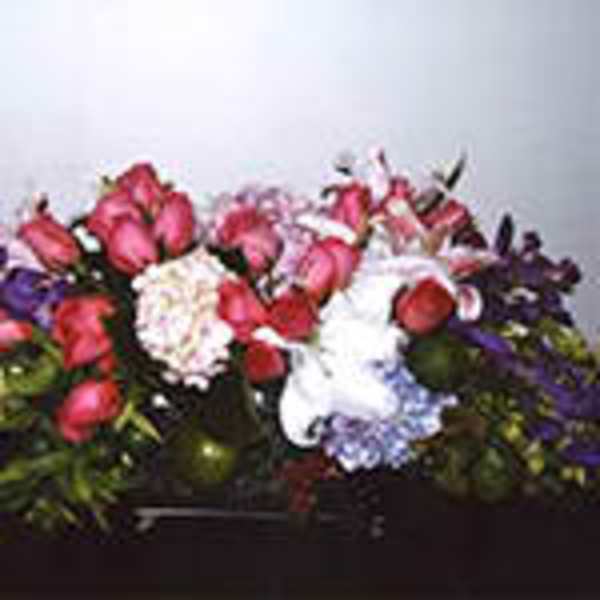 Low, rectangular arrangement of pink roses, white lilies, and mixed blooms in a dark container