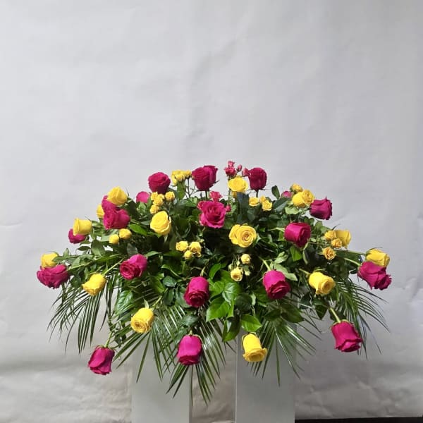 Pink and yellow rose arrangement with palm fronds in a clear stand