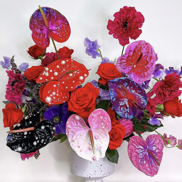 Bold arrangement of red roses and painted anthuriums with pearls in a white speckled vase