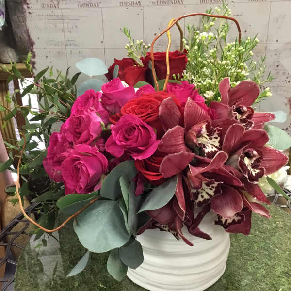 Bouquet of pink and red roses with burgundy orchids in a white vase