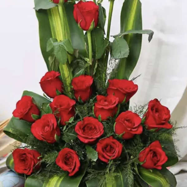 Red roses arranged in a basket with broad green leaves