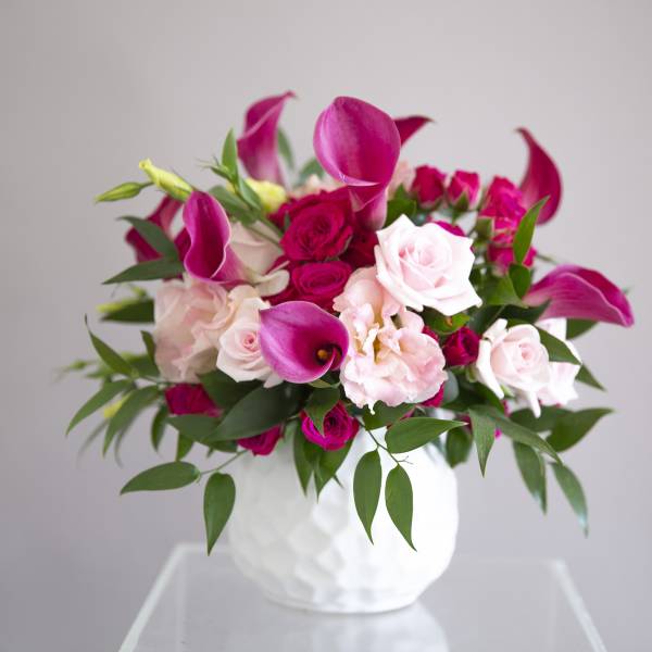Pink and white roses with magenta calla lilies in a white vase