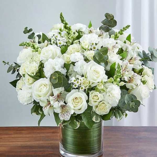 White rose bouquet in a glass vase with green foliage