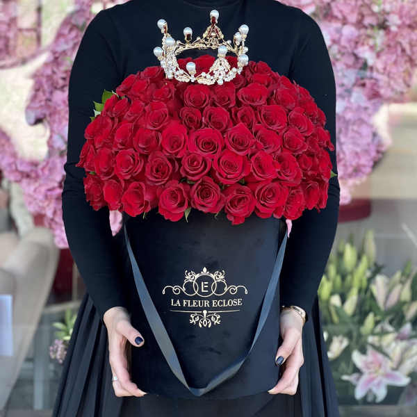 Large red rose arrangement in a black hatbox with a jeweled crown topper