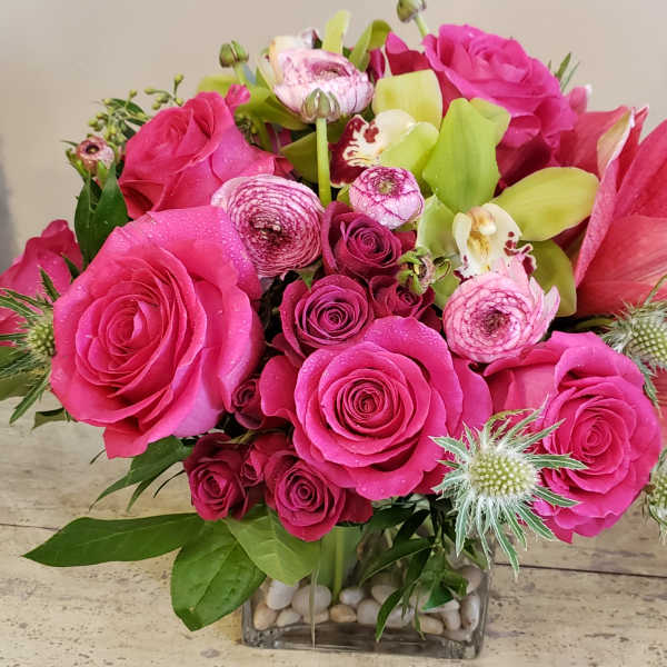Bright pink roses and lilies arranged in a square glass vase.