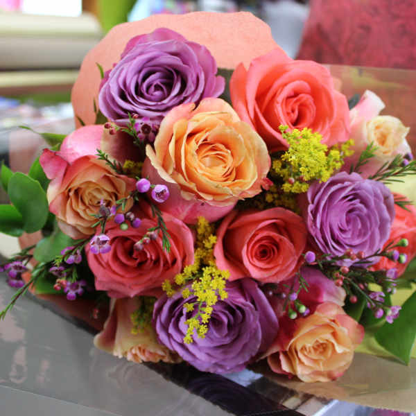 Bouquet of pink, peach, and purple roses with small yellow filler flowers