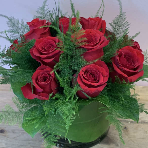 Red roses arranged in a round glass vase with airy greenery