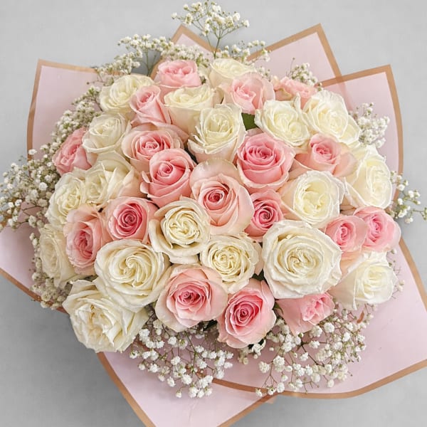 Round bouquet of cream and light pink roses wrapped in pale pink paper with small white filler flowers