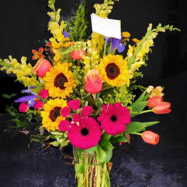 Mixed bouquet with sunflowers, pink gerberas, roses, and tulips in a glass vase