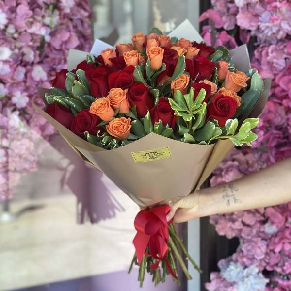 Bouquet of red and peach roses wrapped in tan paper with a red ribbon