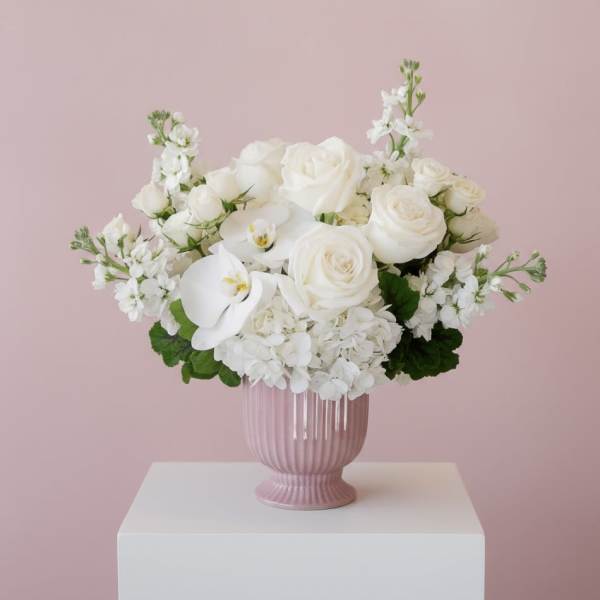 White roses and orchids arranged in a pink vase